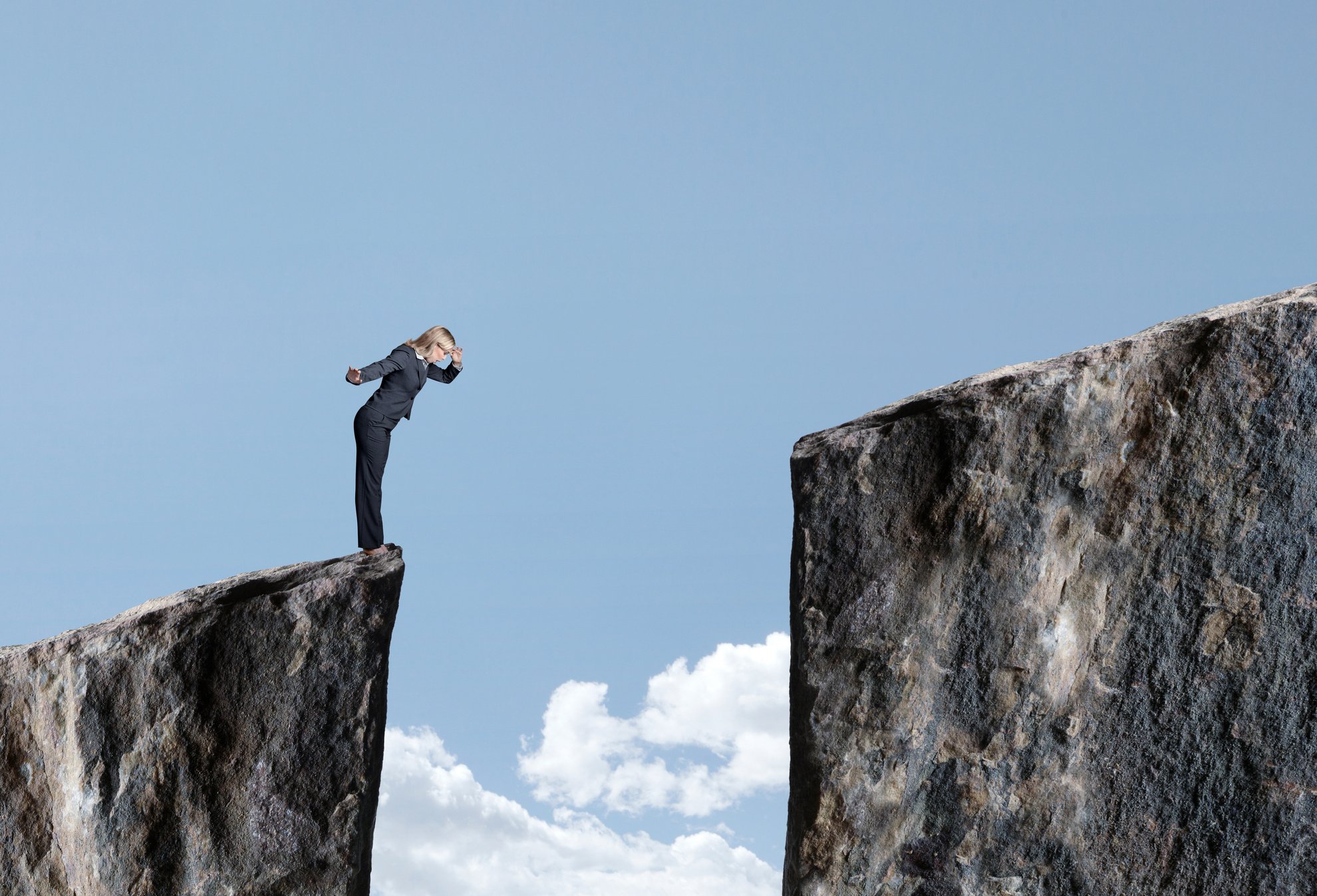 Businesswoman Looks Down At Large Gap Between Two Cliffs