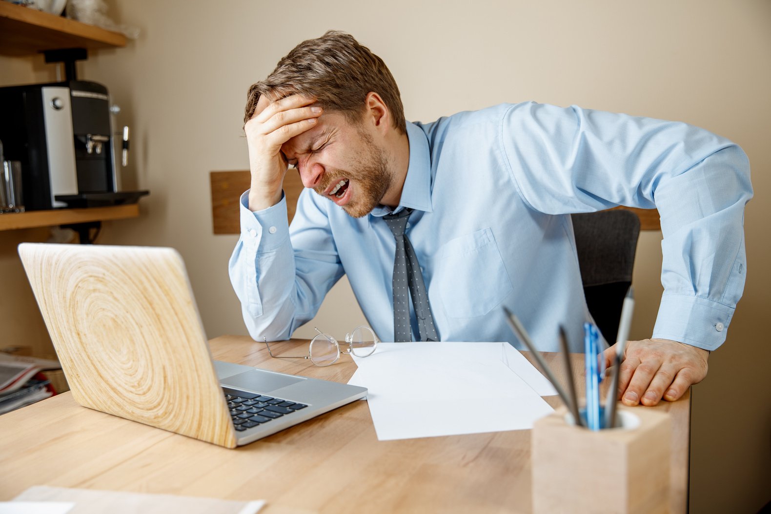 Feeling Sick and Tired. Frustrated Young Man Massaging His Head While Sitting at His Working Place in Office